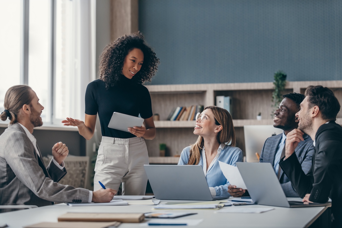 Group of young business people listening to a female speaker while sitting at the office desk together