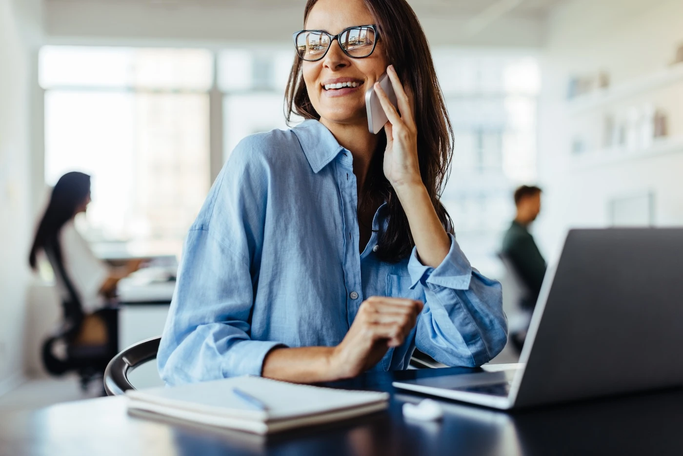 Female business professional making a phone call while sitting in an office. Business woman working with a laptop in a co-working office.
